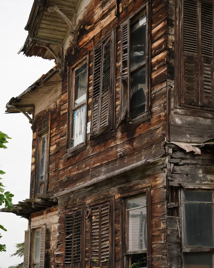 A tall clapboard house gone dark with rot, shutters hanging loose over broken windows.